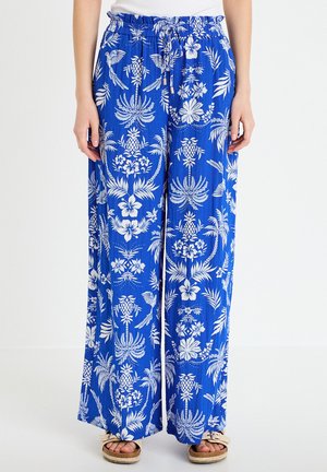 Niebieskie spodnie o szerokich nogawkach z białymi tropikalnymi kwiatowymi i ptasimi wzorami, elastyczna talia z troczkiem, noszone z beżowymi sandałami.