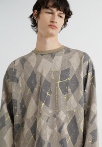 Cămașă cu mâneci lungi dintr-o țesătură gri, având un model geometric cu accente negre și galbene, decolteu rotund și croială relaxată.