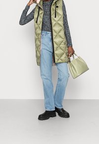 Padded oliwkowa kamizelka z kapturem, czarnymi akcentami i zamkiem; szaro-prążkowana bluzka z długim rękawem; jasnoniebieskie proste dżinsy; czarne masywne buty; jasnooliwkowa torebka.