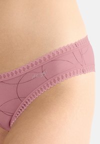 Rosa Spitzen-Panties mit glatter Textur und dezenten kreisförmigen Linienmustern, präsentiert vor einem hautfarbenen Hintergrund.