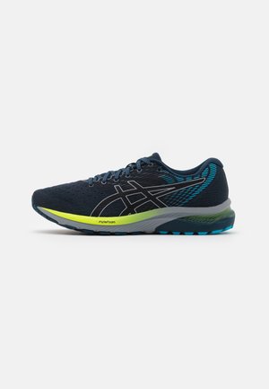 Chaussure de course bleu foncé avec logo noir et bleu, lacets bleus, et semelle à dégradé jaune-vert étiquetée "FlyteFoam".