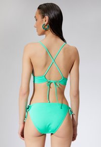 Miętowy bikini z cienkimi, skrzyżowanymi ramiączkami, z zapięciem nawiązanym z tyłu oraz regulowanymi węzłami po bokach dolnej części. Gładki, elastyczny materiał.