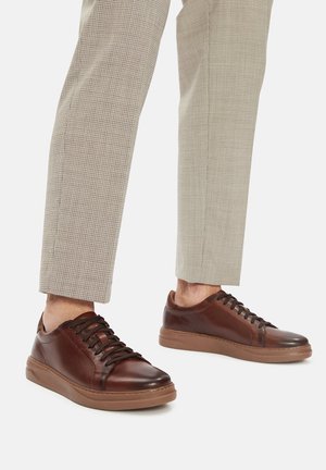 Sneakers in pelle marrone con tomaia liscia, punta rotonda e sistema di allacciatura. La suola è di un tono marrone chiaro a contrasto.