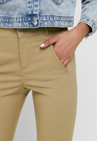 Khakifärgade byxor med en slät yta, utrustade med en framficka och en något avsmalnande ben, tillsammans med en ljusblå denimjacka.