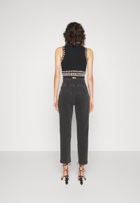 Top corto negro con bordado decorativo, combinado con pantalones negros de tiro alto y corte ajustado, y tacones negros con tiras que presentan acentos circulares.