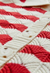 Tissu à motif vichy rouge et blanc avec une surface texturée et trois boutons ronds. Le tissu est épais et fibreux.