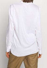 Camicia bianca a maniche lunghe con una sottile texture a righe, dotata di colletto classico e polsini abbottonati, abbinata a pantaloni corti beige.