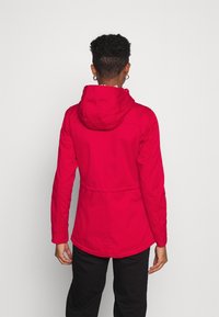 Veste étanche rouge avec capuche, poignets élastiqués, taille à cordon de serrage et texture lisse. Présente un design uni sans motifs.