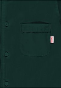 Zielona koszula z guzikami, wykonana z gładkiej tkaniny, z kieszonką na piersi; przy brzegach kieszeni widoczna jest metka z logo "Pockies".