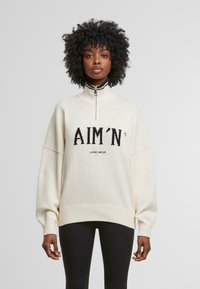 Cream-colored knit sweatshirt with a quarter-zip collar, ribbed hem, and dropped shoulders; features "AIM'N SPORTWEAR" text in black.