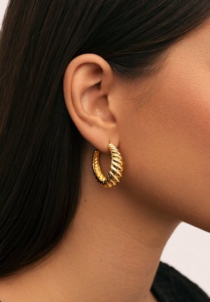 Orecchini a cerchio color oro con un design attorcigliato, caratterizzati da sezioni alternate lisce e rigate. Leggeri, di dimensioni medie e circolari.