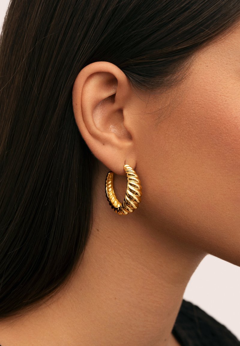 Pendientes de aro en tono dorado con un diseño retorcido, que presenta secciones alternas lisas y acanaladas. Ligeros, de tamaño mediano y circulares.