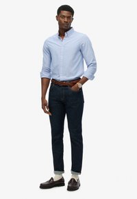 Jasnoniebieska koszula z guzikami w różowe paski, ciemnoniebieskie dżinsy, brązowy pleciony pasek oraz ciemne mokasyny z beżowymi skarpetkami.