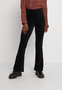 Zwarte fluwelen flared broek met verticale ribbels, met een hoge taille en slim fit, gecombineerd met zwarte platform schoenen.