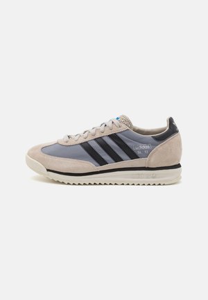 Low-profile Adidas SL 72 sneaker in beige suède en grijs met zwarte strepen, witte zool en vetersluiting, zijaanzicht.