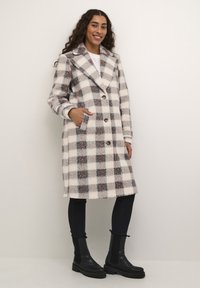 Geruit wollen jas in wit, grijs en roze tinten, met een geknipte kraag, voorzakken en knoopsluiting. Geverfd met zwarte slim-fit broek en laarzen.