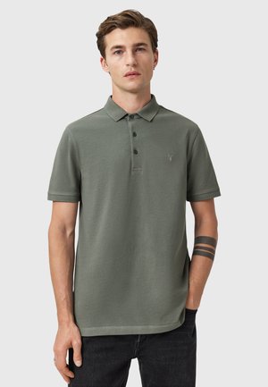 Polo de color verde oliva hecho de algodón, con una tapeta de tres botones, mangas cortas y un logotipo discreto en el pecho.