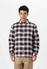 Camisa de cuadros en blanco y negro con acentos en burdeos, con botones en la parte delantera y cuello. Incluye un pequeño logo verde en el pecho. Tejido ligero.