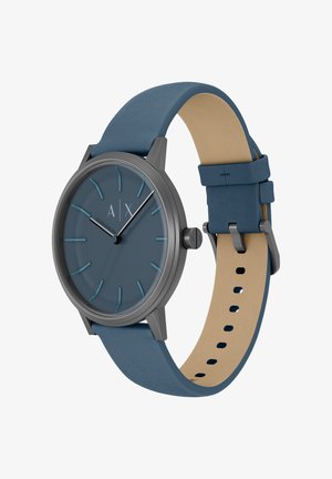 Montre analogique ronde avec un cadran mat bleu foncé, des index argentés, un boîtier en métal gris et un bracelet en cuir bleu avec un dessous beige.