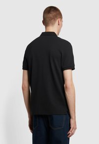 Zwarte polo met een gestructureerde stof, korte mouwen en ribbelkraag. Zijsplitten aan de zoom, getoond op een persoon van achteren.