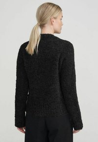 Black textured sweater with long sleeves, round neckline, and a slightly loose fit. Back view reveals a soft, fuzzy material and minimal detailing.
