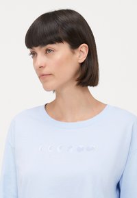Ljusblå sweatshirt med rund halsringning och broderad design av månens faser i vitt över bröstet. Mjuk tygtextur.