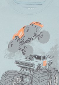 T-shirt bleu clair à manches courtes avec des graphismes de monster truck gris et orange. Tissu en mélange de coton doux avec un design classique à col rond.