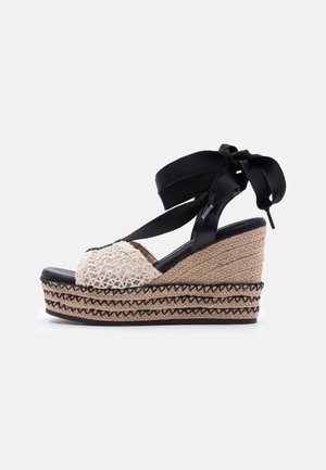 Kileespadrille sandal med sort ankelrem, cremefarvet hæklet foran strop og flettet jute-platformsål med sorte syninger.