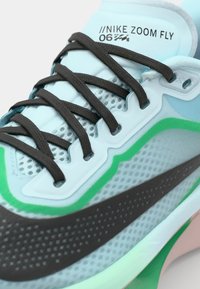 Sneaker Nike Zoom Fly con una toma superiore blu chiaro, lacci marrone scuro e accenti contrastanti verdi e neri con un design testurizzato.