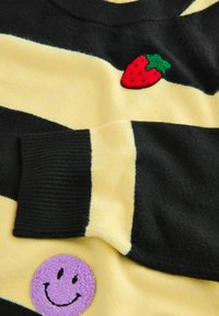 Black and yellow striped sweater featuring a textured red strawberry and a purple smiley face patch. Soft knit material, ribbed cuffs.