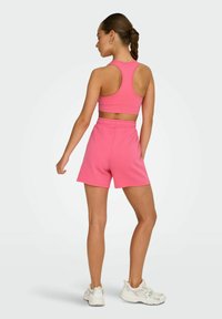 Rosa Sportanzug bestehend aus einem figurbetonten Tanktop mit Racerback-Design und Shorts in mittlerer Höhe; aus glattem, dehnbarem Stoff gefertigt.