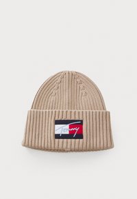 Bonnet en tricot beige avec une texture à côtes. Présente un patch logo en bleu marine, blanc et rouge. Partie supérieure effilée avec un revers.