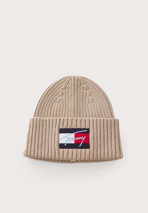 Beige strikket lue med ribbet tekstur. Har et logo-patch i marineblått, hvitt og rødt. Tapered topp med oppbrettet bærestykke.
