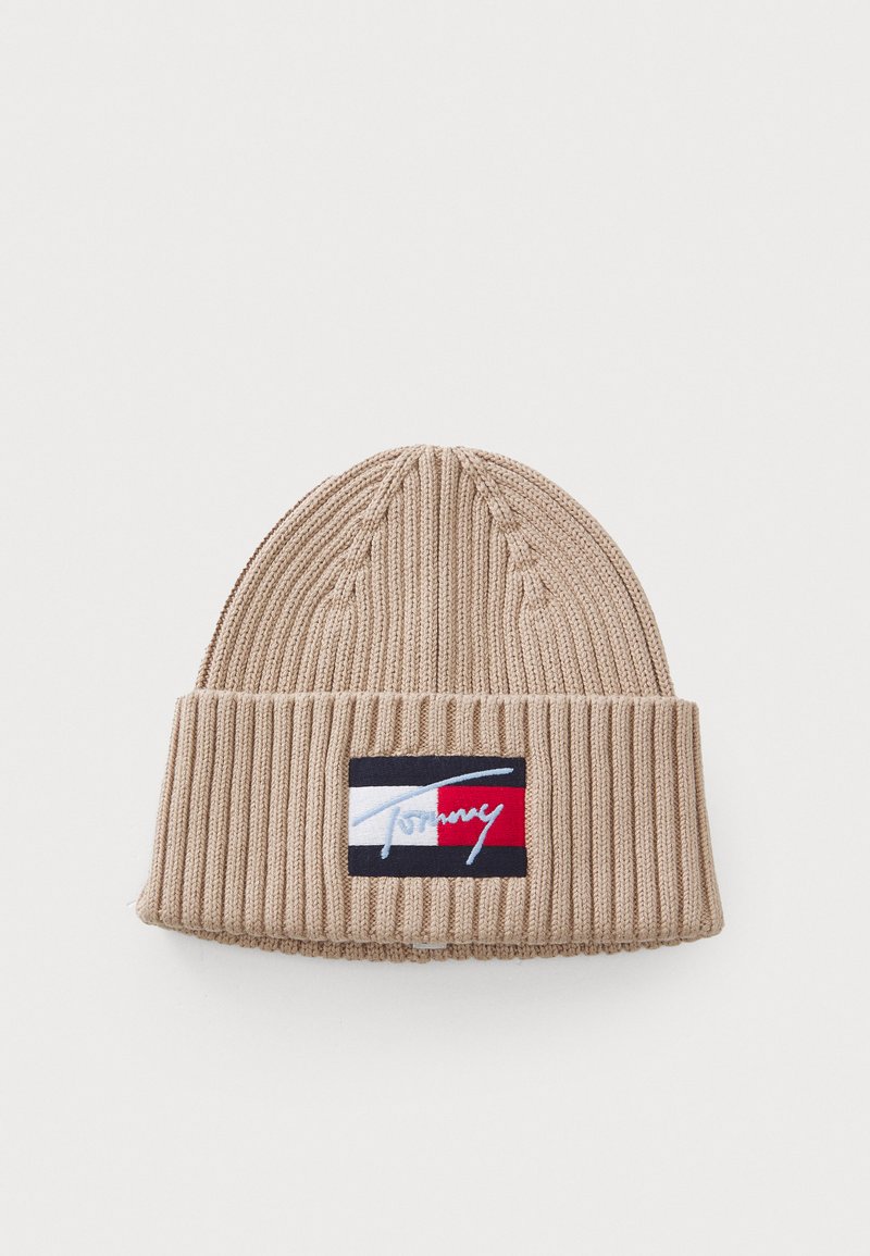 Bonnet en tricot beige avec une texture à côtes. Présente un patch logo en bleu marine, blanc et rouge. Partie supérieure effilée avec un revers.