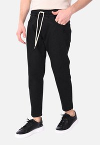 Pantaloni da jogging neri con vita regolabile, tasche laterali e design slim fit. Indossati con sneaker nere con suola bianca.