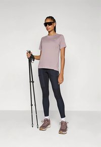 Lys lilla kortermet skjorte, marineblå leggings med lommer, turgåingstaver, og brune sportssko. Solbriller fullfører antrekket.