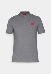 Polo gris hecho de una suave tela de algodón. Presenta un cuello clásico, tres botones y un pequeño parche de marca rojo en el pecho.