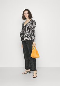 Top zèbre noir et beige avec des manches bouffantes, associé à un pantalon noir plissé. Sac en daim orange et escarpins noirs à lanières.