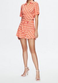 Röd och orange rutigt tvådelat set med en kortärmad topp och en utställd mini-kjol med knytband, bärs med vita snörskor.