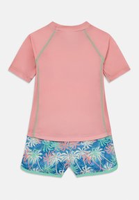 Set rash guarda, ki vsebuje roza zgornji del s kratkimi rokavi in teal poudarki, v kombinaciji z modrimi kratkimi hlačami, okrašenimi s tropskim palmnim vzorcem.
