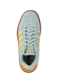 Grijze suède sneaker met drie gele en oranje strepen, vetersluiting en een bruine rubberen zool. Bevat 'adidas' branding op de tong.