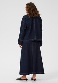 Dunkelblaue Jeansjacke und Rock mit kontrastierenden Nähdetails. Das Outfit hat eine lockere Passform, mit einem langen Rock, der bis zu den Knöcheln reicht.