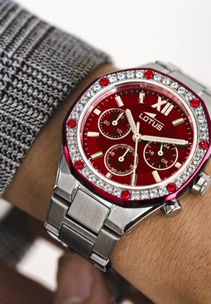 Rode roestvrijstalen horloge met een bezel versierd met edelstenen, achtzijdige vorm en chronograaf functies. Zilveren metalen band met geborstelde textuur.