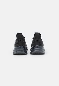 Zapatillas deportivas negras con un tejido de punto texturizado, suela de goma, lengüetas en el talón trasero y acentos reflectantes. Diseño minimalista con un acolchado pronunciado.