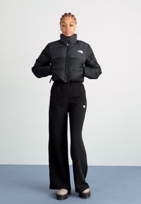 Černá péřová bunda s vysokým límcem a předním zipem, spárovaná s upnutými černými tepláky. Oblečení má minimalistický design.