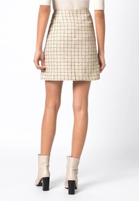 Minigonna checkered beige e nera realizzata in tessuto testurizzato, con taglio dritto e zip nascosta sul retro.