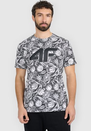 Mężczyzna z brodą, ubrany w czarno-biały T-shirt z motywem koszykówki i dużym logo "4F", stoi na jednolitym jasnym tle.