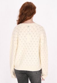 Krém színű köt�ött pulóver nyitott gyémántmintával, hosszú ujjal és laza fazonnal. Bordás alsó rész és mandzsetta, könnyű textúrával.