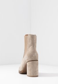 Botín beige hasta el tobillo con tacón cuadrado, hecho de un material similar al ante. Presenta paneles laterales elásticos y una textura suave.