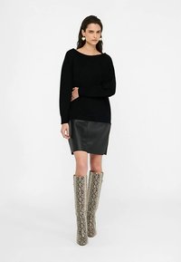 Sort langærmet sweater, sort nederdel i imiteret læder og knælange støvler med slangeprint. Glatte stoffer med en tætsiddende silhuet.